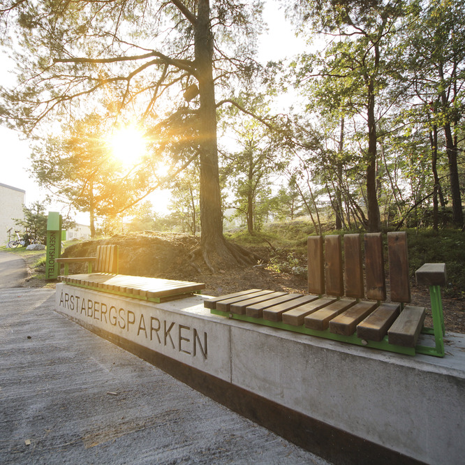 Längs en betongmur finns sittplatser. Parkens namn är skrivet på muren.